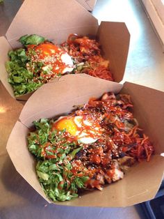 two takeout boxes filled with food sitting on top of a counter