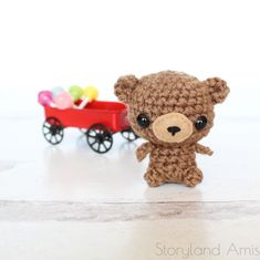 a crocheted teddy bear next to a red wagon with candy on the wheels