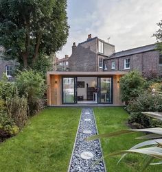 a modern house with an outdoor garden and gravel path leading to the front door, surrounded by greenery