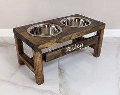 two metal bowls on a wooden stand with the word riley written in white lettering below