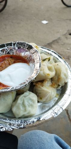 a person holding a silver plate with dumplings and sauce on it's side