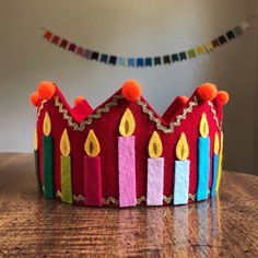 a crown made out of felt with lit candles on the front and sides, sitting on a table