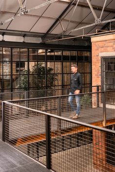 a man walking across a bridge in front of an open air area with metal railings