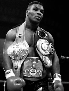 professional boxer mike tyson standing in the ring with his belts around his waist and looking at the camera