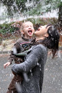 a woman holding a small child in her arms while it rains down on the ground