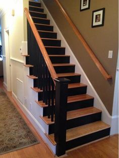 a stair case with black and white railings next to a wooden handrail in a home