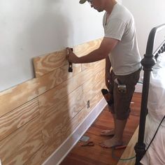 a man in white shirt and khaki pants working on wood paneling next to bed