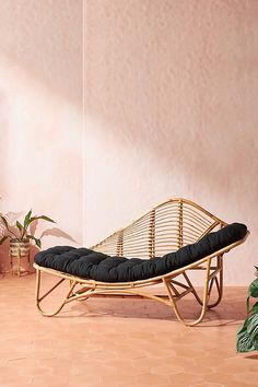 a rattan chaise lounge chair with black cushions in front of a pink wall