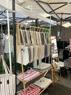 an outdoor market with clothes and handbags for sale under a tented awning