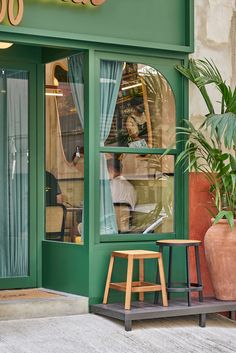 a person sitting at a table in front of a green storefront with the window open