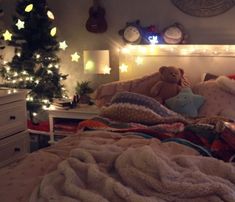 a teddy bear sitting on top of a bed next to a christmas tree and lights