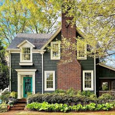 a gray house with white trim and blue door in the front yard is surrounded by trees