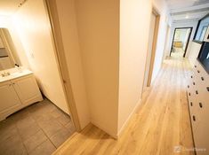 an empty hallway leading to a bathroom with white cabinets and wood flooring on the walls