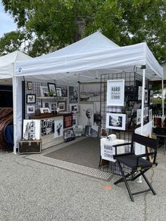 a white tent with pictures on the wall and chairs under it in front of trees