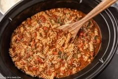 a wooden spoon in a slow cooker filled with pasta and tomato sauce, ready to be cooked