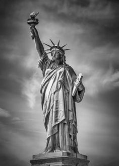 the statue of liberty is shown in black and white with cloudy skies behind it on a sunny day