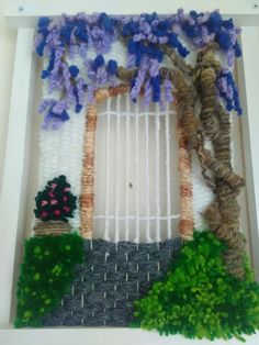 an art work made out of yarn with flowers and trees on the outside, in a white frame