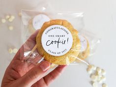 a hand holding a cookie with congratulations sticker on it's wrapper next to white candies