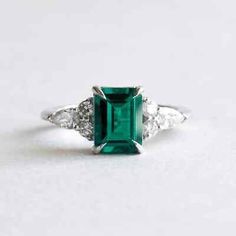 an emerald and diamond ring with three diamonds on the side, set in white gold