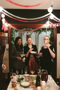 three women standing around a table with plates and drinks