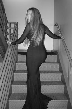 a woman in a long black dress is walking down the stairs with her arms outstretched