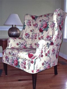 a flowered chair in a living room with a lamp on the end table next to it