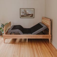 a wooden bed frame sitting on top of a hard wood floor next to a plant