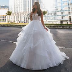 a woman in a white wedding dress is standing on the street with tall buildings behind her