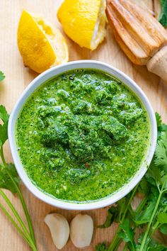 a white bowl filled with green pesto next to sliced lemons and parsley