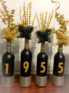 three black bottles with gold numbers on them and some flowers in the top one is filled with beads