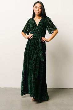 a woman in a green velvet dress standing with her hands on her hips and looking at the camera