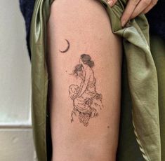 a woman with a small tattoo on her thigh holding a baby in her arms and the moon behind her