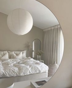 a large white bed sitting under a round mirror