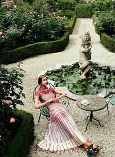 a woman sitting on a chair in front of a pond with water lilies and roses