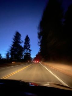 a car driving down the road at night with its lights on and trees in the background