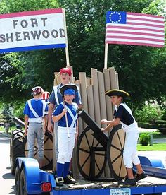 two boys are standing on the back of a truck with an american flag in the background