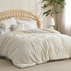 a bed with white comforter and pillows in a room next to a plant on the floor