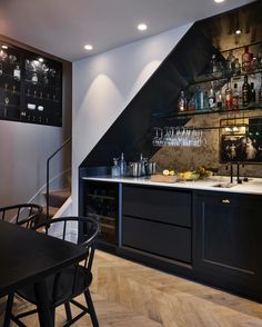 a kitchen with black cabinets and shelves filled with wine glasses on the bar counter top