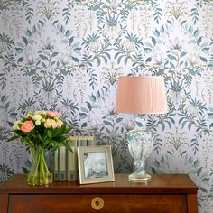 a vase with flowers on top of a dresser next to a lamp and photo frame