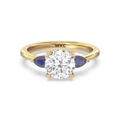 a yellow gold engagement ring with two blue sapphire stones on the band and an oval cut diamond