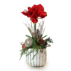 a white vase filled with red flowers and greenery next to a christmas ornament