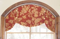 an arched window with red and gold floral curtain valance in front of the window