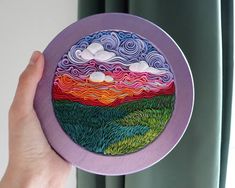 a hand holding a purple plate with an image of mountains and clouds painted on it