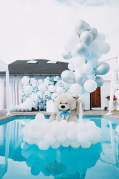 a teddy bear sitting in the middle of a pool surrounded by white balloons and streamers