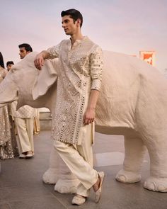 a man standing next to an elephant statue in front of other people wearing white outfits