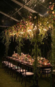 a long table set up with flowers and greenery for an outdoor dinner party at night