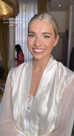 a woman with blonde hair wearing a white robe and smiling at the camera while sitting down