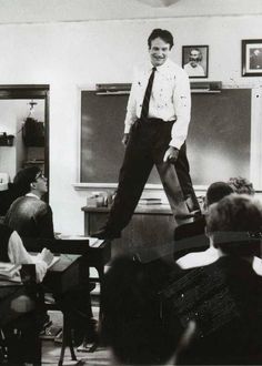 a black and white photo of a man standing in front of a class room full of students