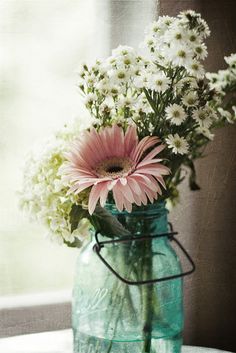 a vase filled with white and pink flowers on top of a table next to a window