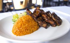 a white plate topped with meat and rice next to broccoli on a table